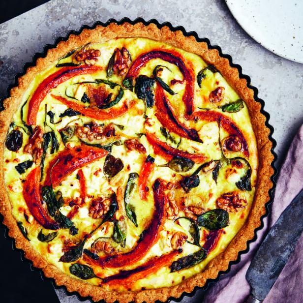 Eine Quiche mit Paprika, Spinat, Feta und Walnüssen auf einem Tisch.