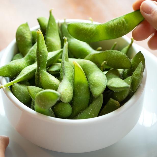 Eine Hand nimmt eine Edamame-Schote aus einer Schüssel.