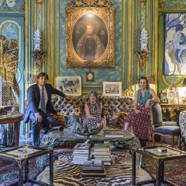 Drei Personen sitzen in einem opulenten Wohnzimmer mit Gemälden und Antiquitäten.