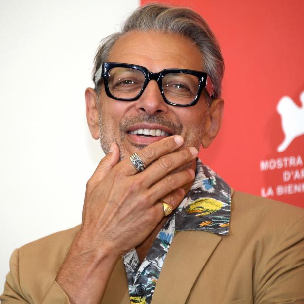 Jeff Goldblum mit Brille posiert vor einem roten Hintergrund.