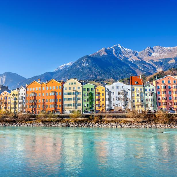 Bunte Häuserzeile am Ufer des Inns in Innsbruck vor einer Bergkulisse.