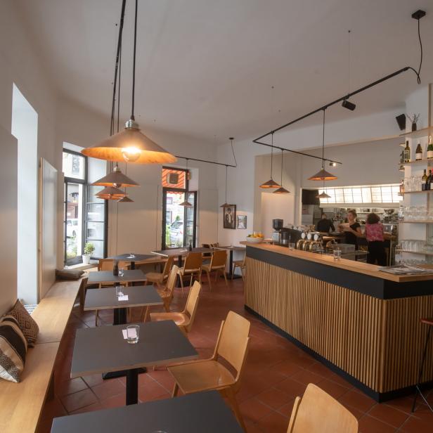 Innenansicht eines Restaurants mit Tischen, Stühlen und einer Bar.