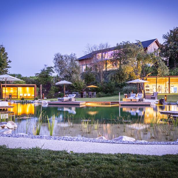 Ein luxuriöses Resort mit einem See, kleinen Häusern und Liegeflächen im Freien bei Dämmerung.