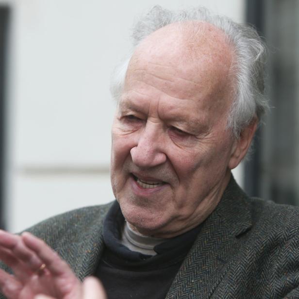 Ein älterer Mann mit grauem Haar gestikuliert mit der Hand.