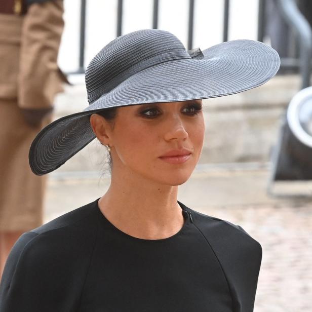 Meghan, Herzogin von Sussex, trägt einen schwarzen Hut und ein schwarzes Kleid.