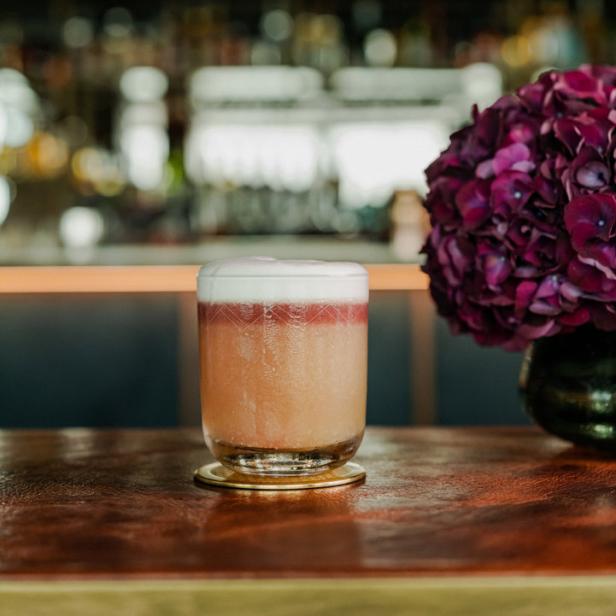 Ein Cocktail mit Schaumkrone steht auf einer Bar neben einer lila Hortensie.