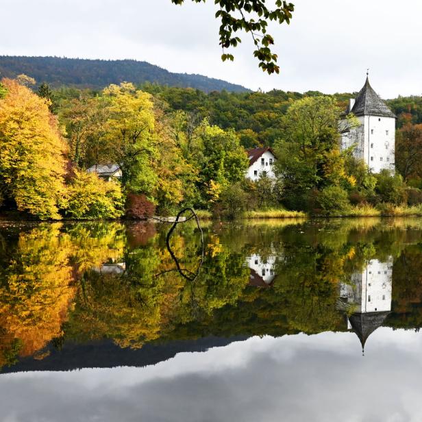 Ein weißes Schloss spiegelt sich in einem ruhigen See, umgeben von Herbstlaub.