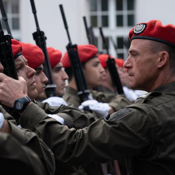 Eine Reihe von Soldaten in Uniform und roten Baretts steht mit Gewehren in Reih und Glied.