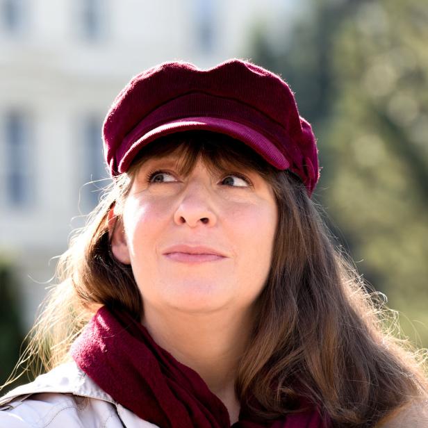 Eine Frau mit braunen Haaren, einem roten Hut und einem passenden Schal blickt nach oben.