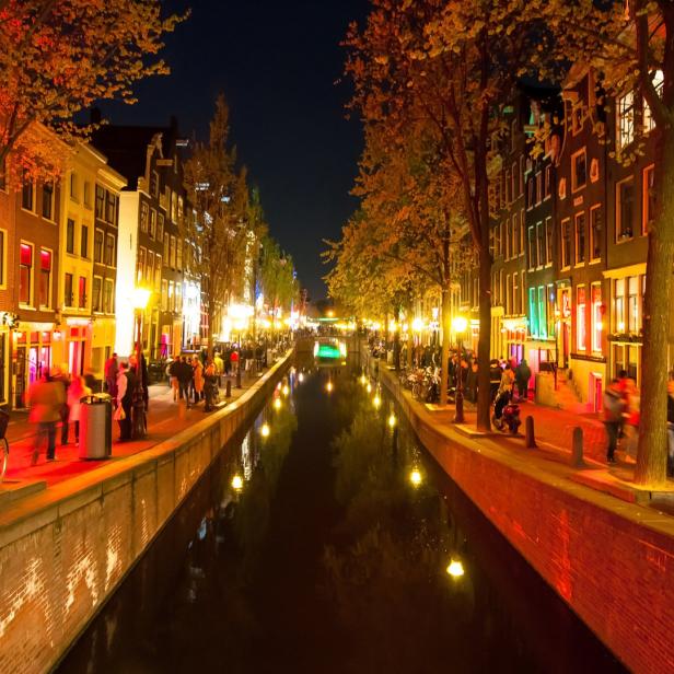 Ein Kanal in Amsterdam bei Nacht mit beleuchteten Gebäuden und Menschen.