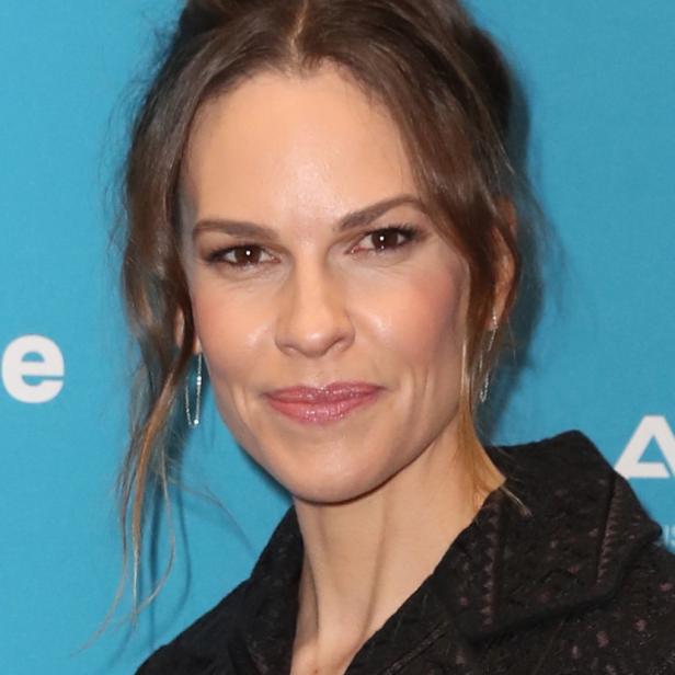 Ein Porträt von Hilary Swank vor einem hellblauen Hintergrund.
