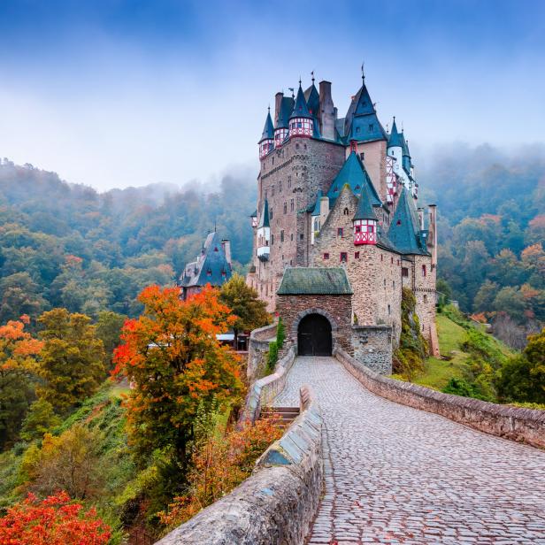 Die Burg Eltz thront auf einem Hügel, umgeben von herbstlichen Wäldern.
