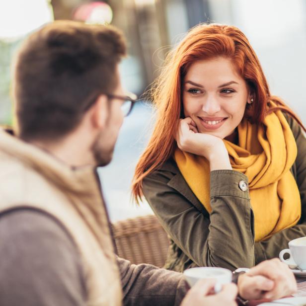 Eine Frau mit roten Haaren lächelt einen Mann in einem Café an.