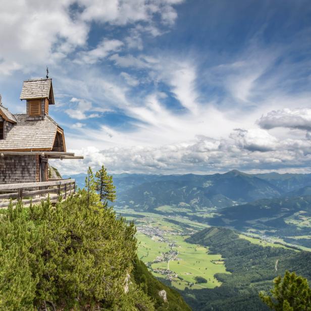 Die kleine, hölzerne Bergkapelle thront auf einem Felsen mit Blick auf das grüne Tal.