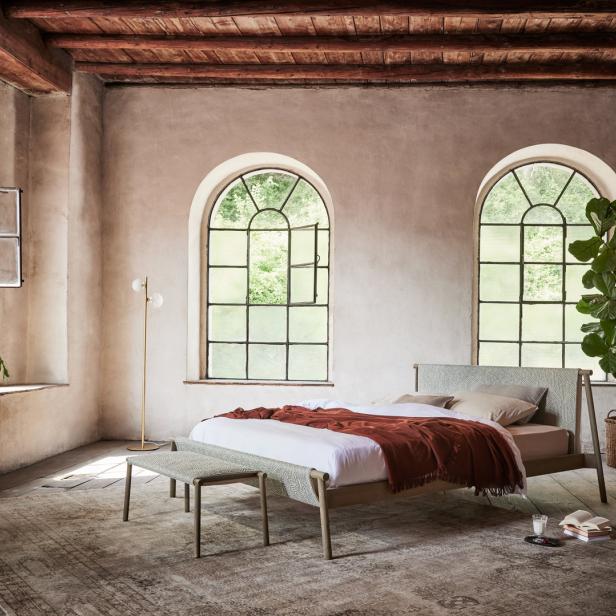 Ein Schlafzimmer mit einem Bett, zwei großen Fenstern und Zimmerpflanzen.