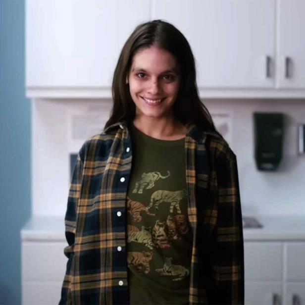 Eine lächelnde junge Frau mit einem T-Shirt mit Tigermotiv steht in einem Raum mit Schränken.