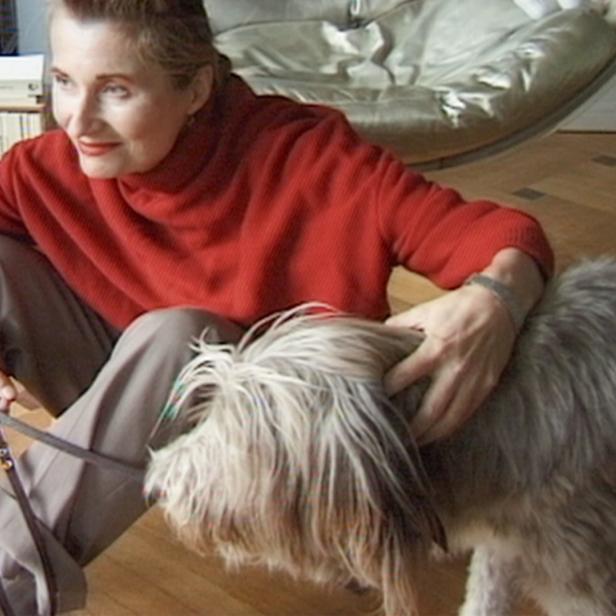 Eine Frau sitzt auf dem Boden und streichelt ihren zotteligen Hund.