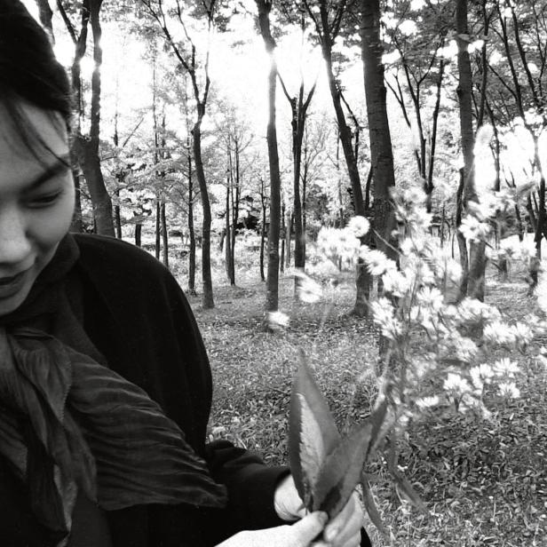 Eine Frau betrachtet einen Strauß weißer Blumen in einem Wald.