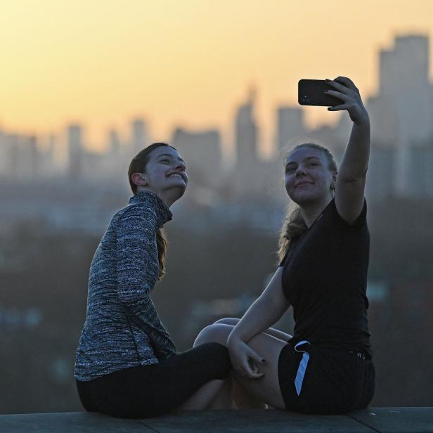 Zwei junge Frauen machen ein Selfie vor einer Skyline im goldenen Abendlicht.