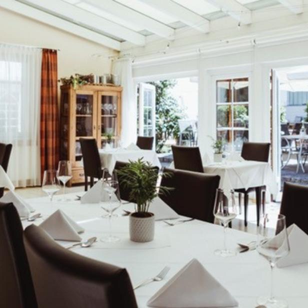 Ein helles Restaurant mit weiß gedeckten Tischen und dunklen Stühlen.