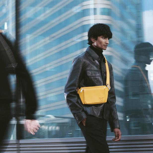 Ein Mann mit einer gelben Louis Vuitton-Tasche vor einem Bürogebäude.