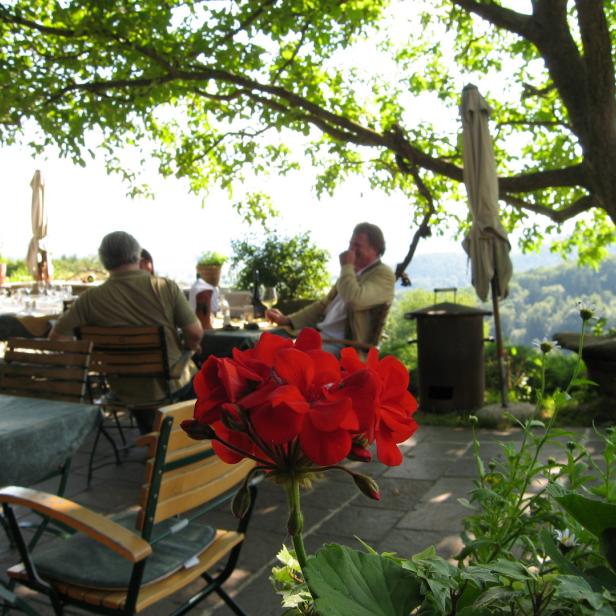Ein Restaurant im Freien mit Gästen unter einem schattenspendenden Baum.