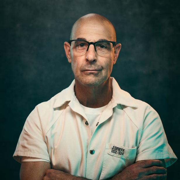 Stanley Tucci in einer hellen Uniform mit verschränkten Armen.