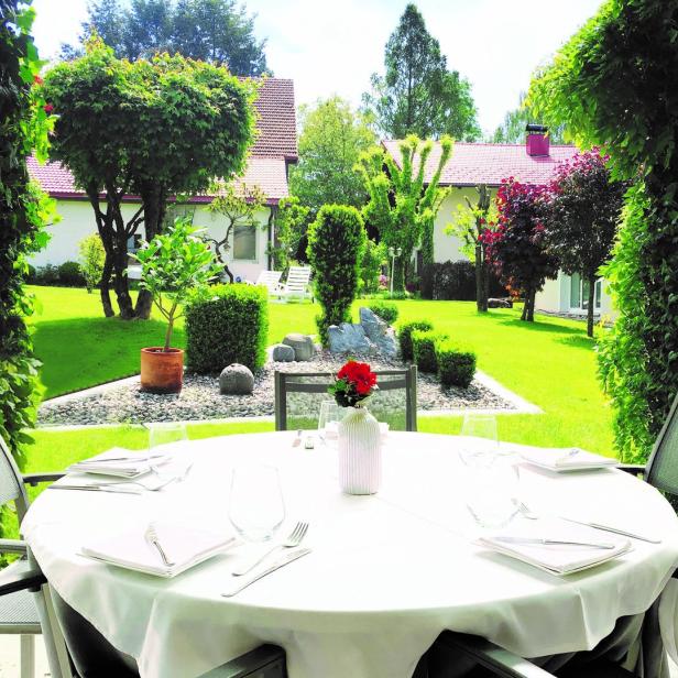 Ein gedeckter Tisch auf einer Terrasse mit Blick auf einen gepflegten Garten.