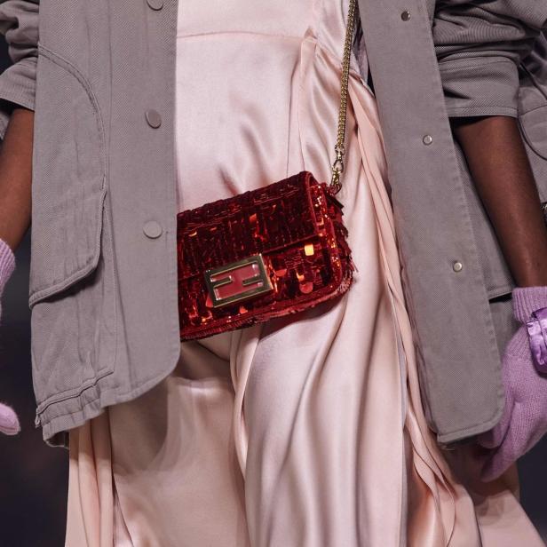 Eine Person mit einer roten Fendi-Tasche und lila Handschuhen.