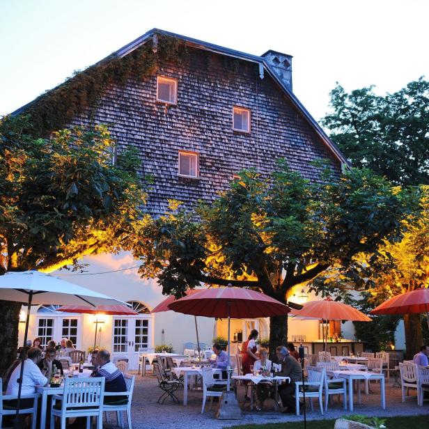 Ein Restaurant mit Tischen und Sonnenschirmen im Freien vor einem großen Gebäude.
