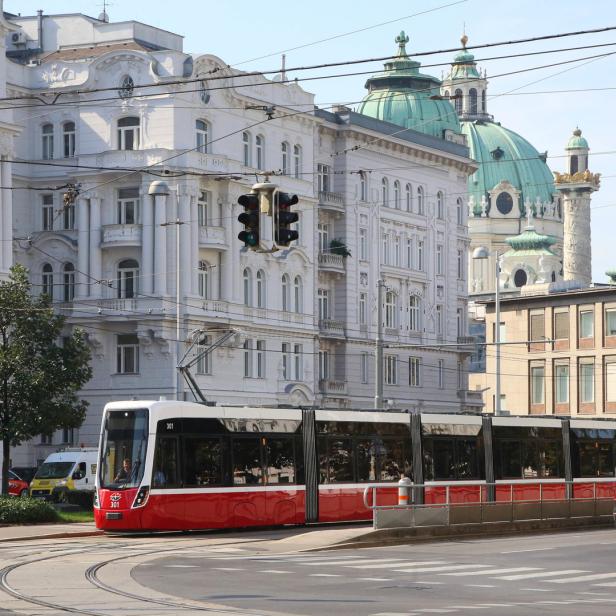 Eine rote Straßenbahn fährt durch Wien, im Hintergrund die Karlskirche.