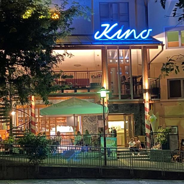 Ein Kino mit Außenbereich und blauem Neonschild bei Nacht.