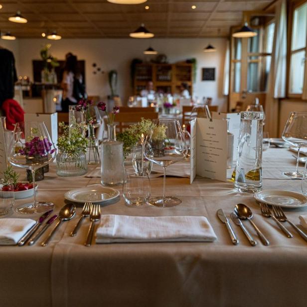 Ein festlich gedeckter Tisch in einem Restaurant mit Gläsern, Geschirr und Blumenarrangements.