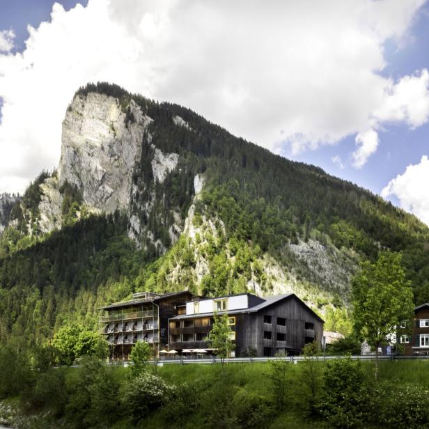 Ein Hotel liegt vor einem bewaldeten Berg mit einer markanten Felswand.