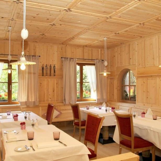 Ein holzgetäfelter Gastraum mit gedeckten Tischen und Fensterplätzen.
