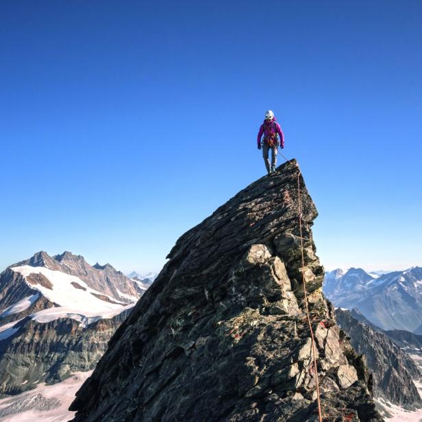 Eine Bergsteigerin steht auf einem Gipfel mit Blick auf schneebedeckte Berge.