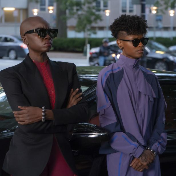 Okoye und Shuri, zwei Charaktere aus dem Film „Black Panther: Wakanda Forever“, posieren vor einem Auto.