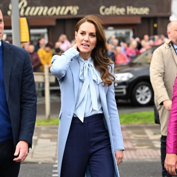Prinzessin Kate überquert eine Straße in einem hellblauen Mantel und marineblauer Hose.