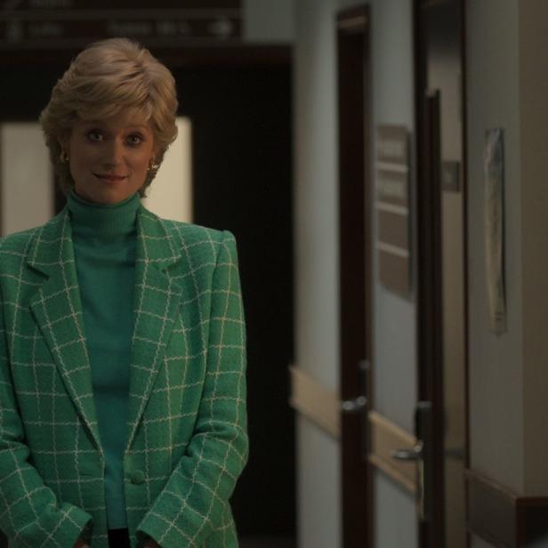 Eine Frau mit blonden Haaren und grünem Blazer steht in einem Flur.