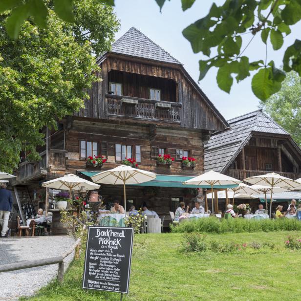 Ein traditionelles Holzhaus mit Gästen, die unter Sonnenschirmen sitzen und speisen.