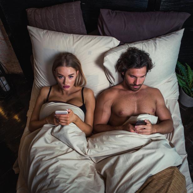 Ein Paar liegt im Bett und schaut auf ihre Smartphones.