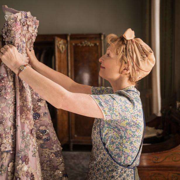 Eine Frau betrachtet ein aufwendig verziertes, hellviolettes Kleid.