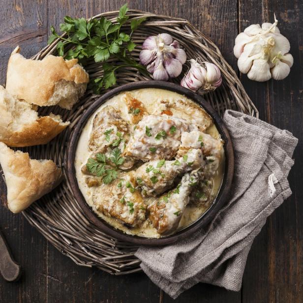 Hähnchen in cremiger Sauce mit Brot, Knoblauch und Petersilie auf einem rustikalen Holztisch.