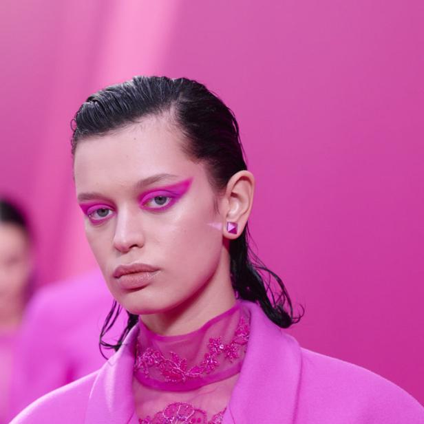 Ein Model mit pinkfarbenem Blazer und auffälligem, pinkfarbenem Augen-Make-up vor pinkfarbenem Hintergrund.
