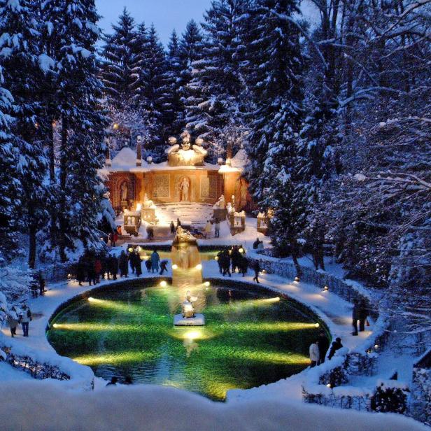 Ein schneebedeckter Park mit einem beleuchteten Teich und einem verzierten Gebäude im Hintergrund.
