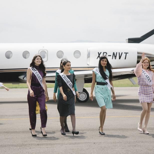 Mehrere Schönheitsköniginnen mit Schärpen und Diademen gehen vor einem Privatjet entlang.