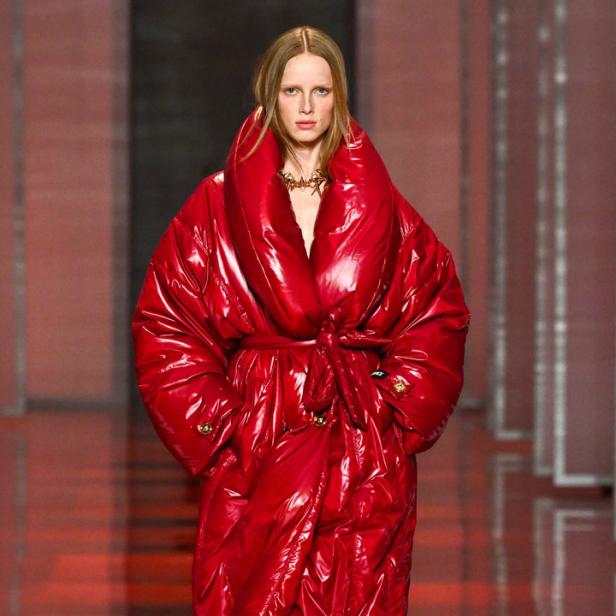 Ein Model präsentiert einen glänzenden, roten Daunenmantel mit passenden Stiefeln auf dem Laufsteg.