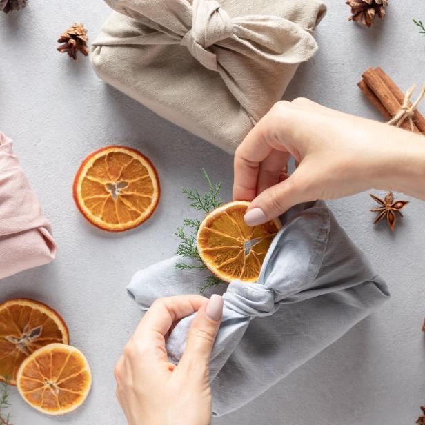 Eine Person dekoriert ein Geschenk, das in Stoff gewickelt ist, mit einer getrockneten Orangenscheibe.