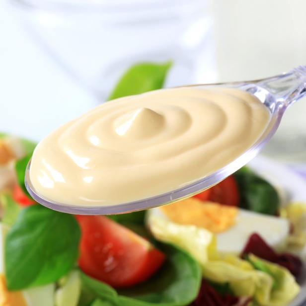 Ein Löffel mit cremiger Sauce über einem Salat mit Tomaten und Ei.