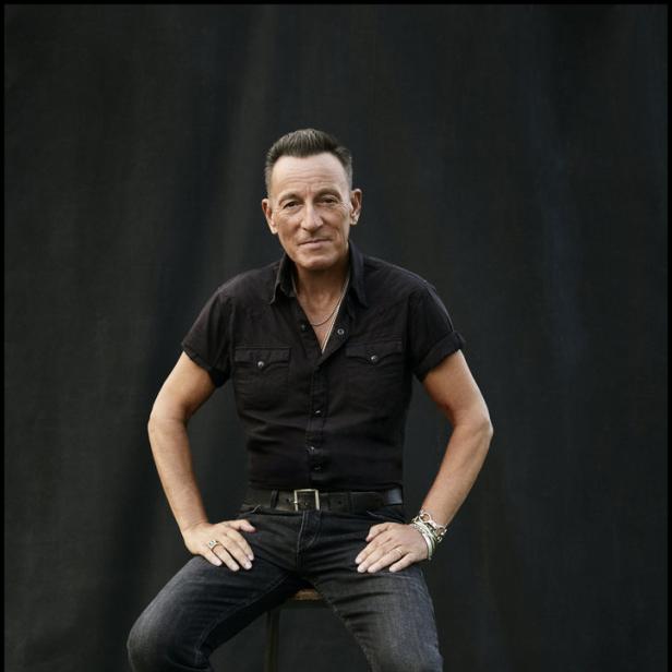 Bruce Springsteen sitzt auf einem Hocker vor einem schwarzen Hintergrund.